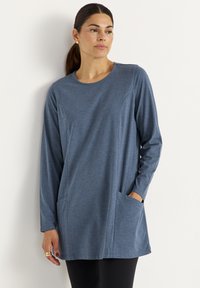 Langärmlige Tunika aus mittlerem blauen Stoff mit Rundhalsausschnitt und Seiten Taschen, die eine schlanke, lässige Passform und eine glatte Textur aufweist.