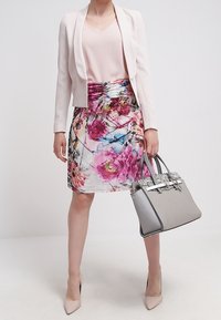 Blazer rose pâle à manches longues, haut pastel, jupe à motifs floraux dans des tons de rose et de bleu, et sac à main gris avec des ferrures en argent.