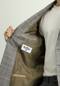 Grijze geruite blazer met beige voering, binnenzak en label. Heeft een soepele textuur en een gestructureerd ontwerp.