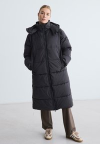 Czarna kurtka puchowa o długim, oversize'owym fasonie, z pionowymi przeszyciami, wysokim kołnierzem i zamkiem błyskawicznym z przodu. Posiada boczne kieszenie oraz kaptur.