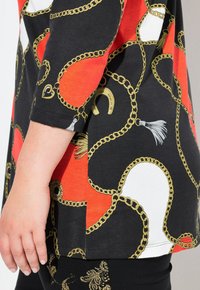 Schwarzes T-Shirt mit goldenen Ketten- und Hufeisenmustern auf einem orange-weißen Hintergrund, mit lässigem Schnitt und Dreiviertelärmeln.