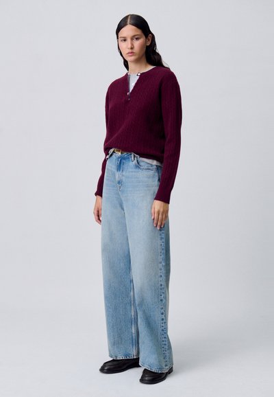 Pull en tricot bourgogne avec décolleté en V et texture côtelée, associé à un jean en denim large bleu clair et des bottines noires.