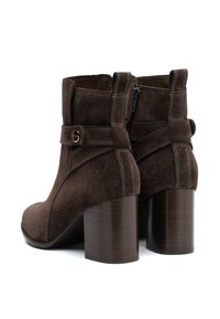 Botine din suede maron cu toc pătrat, având fermoar lateral, detalii cu curea și cusături în contrast.