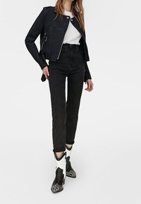 Giubbotto da biker in suede nero con dettagli in cerniera silver, jeans neri a vita alta e stivali alla caviglia con un design misto in bianco e nero.