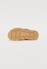 Sandale avec une semelle en caoutchouc beige, présentant une surface texturée et une adhérence en motif pour une meilleure traction. Conçue pour le confort et la stabilité.