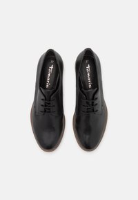 Chaussures en cuir noir à texture lisse, bout arrondi et design à lacets. Semelles en caoutchouc marron et logo de la marque visible à l'intérieur. Taille 37.