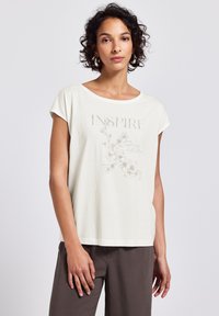 Lyscreme bomulds t-shirt med bred halsudskæring, korte ærmer og et blomstermotiv med ordet "INSPIRER" i tekstureret skrift.