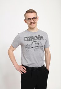 Šedé bavlněné tričko s černou grafikou designu a rozměrů automobilu Citroën, v kombinaci s černými kalhotami a černým pásem.
