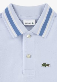 Ανοιχτό μπλε πόλο πουκάμισο με υφή υφάσματος, δύο κουμπιά και ριγέ γιακά σε ανοιχτό μπλε και λευκό. Διαθέτει πράσινο κεντημένο λογότυπο.