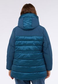 Tyrkysová péřová bunda s kapucí, která má prošívaný design a hladký povrch. Disponuje vodorovným švem a mírně delší zadní částí.