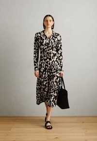Abito a maniche lunghe con stampa animale nera e panna, dotato di una parte frontale con bottoni e una silhouette fluida. Abbinato a una borsa a spalla nera.