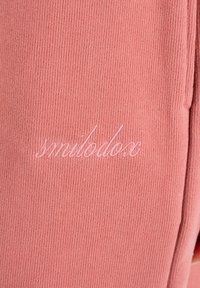 Zbliżenie na różowy, prążkowany materiał z jasnoróżowym kursywym haftem przedstawiającym napis „smilealove” na powierzchni.