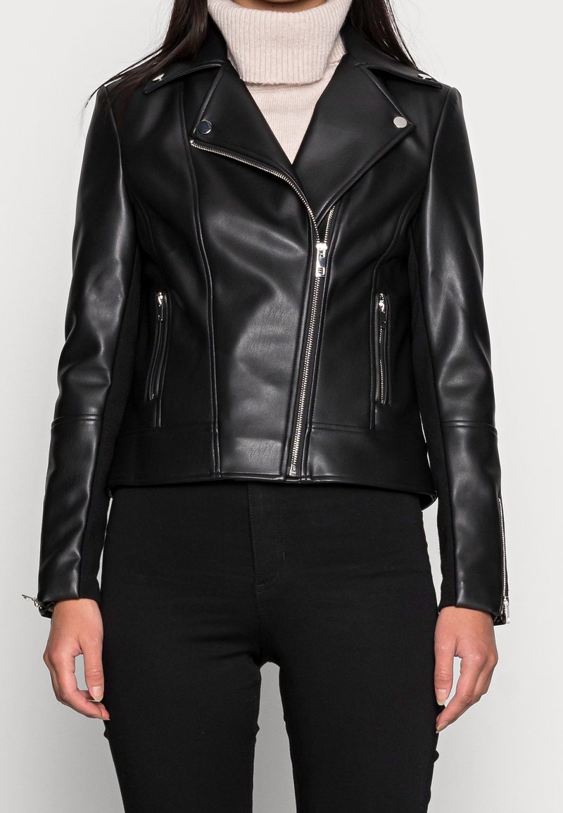 Giubbotto da motociclista in pelle nera con accessori in argento, tasche con zip e design aderente. Presenta un colletto affilato e una superficie liscia.