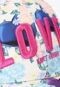 Pet met bloemenpatroon en opvallende roze letters "LOVE", blauwe hartaccenten en merknaam "Kurt Geiger" in het roze, met een textuurstof oppervlak.
