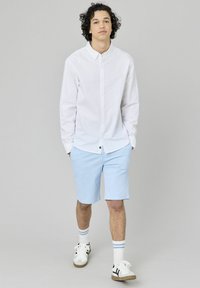 Chemise blanche à boutons, shorts bleu clair, baskets blanches avec accents noirs, et chaussettes blanches avec rayures bleues disposées soigneusement.