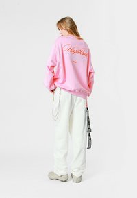 Sudadera oversized rosa con "Unfiltered" en letras naranjas, combinada con pantalones holgados blancos y calzado gris. Detalles de cadena de plata visibles.