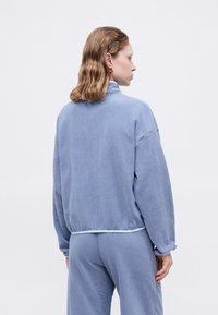 Svetlomodrý fleece pulóver s vysokým golierom, voľným strihom a rebrovaným lemom. Obsahuje spustené ramená a mäkkú, textúrovanú látku.