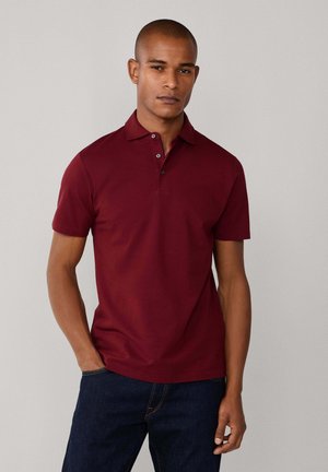 Polo bourgogne à manches courtes, avec un col à deux boutons et une texture lisse. Assorti avec un jean en denim foncé.