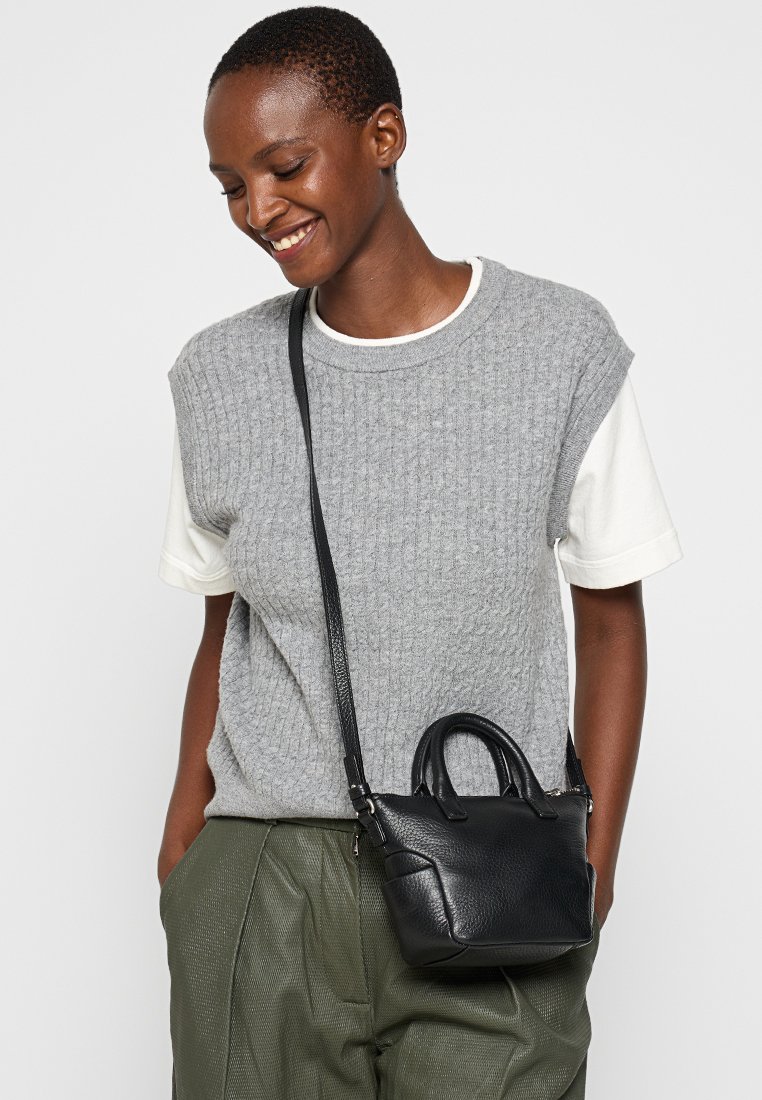 Mała czarna skórzana torebka z dwoma uchwytami i regulowanym paskiem na ramię. Posiada teksturowane wykończenie i zwarty, usztywniony kształt.