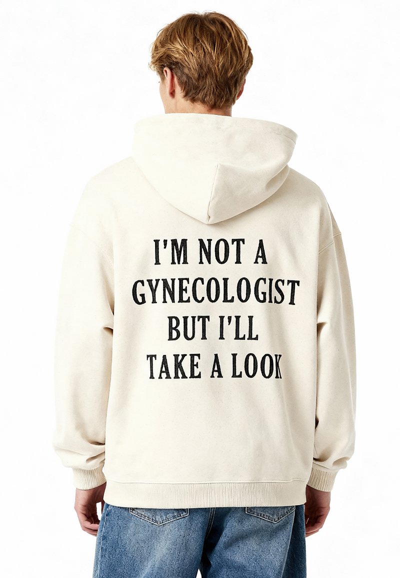Felpa beige con una grande stampa sul retro in testo nero che recita: "NON SONO UN GINECOLOGO MA DARÒ UN'OCCHIATA." Materiale morbido, vestibilità casual.