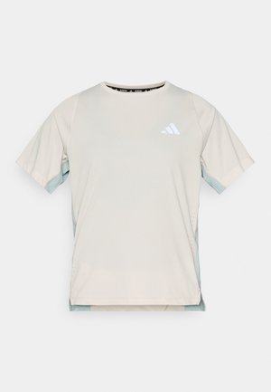 Gaiši bēša sporta t-krekls ar īsām piedurknēm, sānos ar tirkīza krāsas paneli un baltu logo uz krūtīm. Gluda tekstūra.