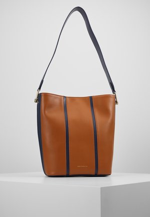 Brązowa skórzana torba kubełkowa z pionowymi granatowymi paskami i pojedynczym granatowym paskiem na ramię, prezentowana na białym postumencie na jasnym tle.