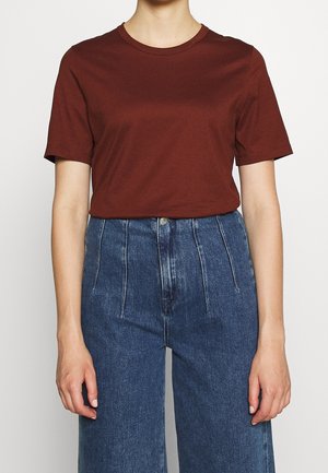 Person iført en ensfarvet mørkerød kortærmet T-shirt, der er stoppet ned i højtaljede blå jeans med lodrette sømme.