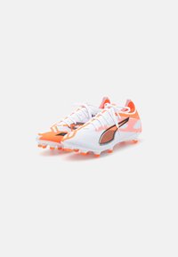 White soccer cleats with orange accents and black details, featuring a mesh upper, lace closure, and textured rubber studs for traction.