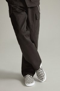 Pantalones cargo negros con bolsillos laterales y un ajuste holgado, combinados con zapatillas de cuadros en blanco y negro. Tejido suave y diseño casual.