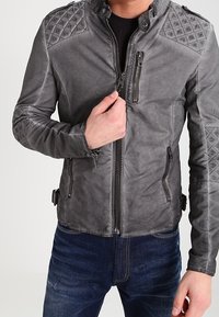 Giubbotto di pelle grigio con spalle a motivo a diamante, tasche laterali e chiusura con zip. Presenta cinturini regolabili in vita.