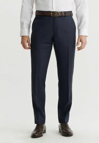 Granatowe spodnie wizytowe o dopasowanym kroju, z drobną fakturą i przodu z zakładkami. Połączone z brązowym skórzanym paskiem i brązowymi butami z detalami typu wingtip.