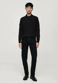 Zwarte zip-neksweater gecombineerd met slim-fit zwarte broek en zwarte schoenen. De outfit heeft een naadloos, textuur ontwerp.