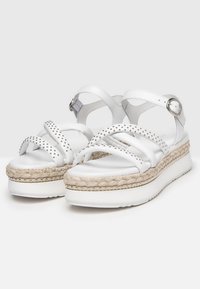 Sandali platform bianchi con suola intermedia intrecciata simile al juta, borchie metalliche decorative e cinturino alla caviglia regolabile, con parte superiore in sintético liscia.
