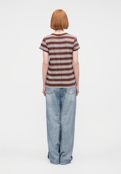 Καφέ και λευκό ριγέ t-shirt με κοντά μανίκια και χαλαρή εφαρμογή, συνδυασμένο με ανοιχτό μπλε τζιν παντελόνι με φαρδιά μ πατζάκια, με ορατή ραφή στην πλάτη.