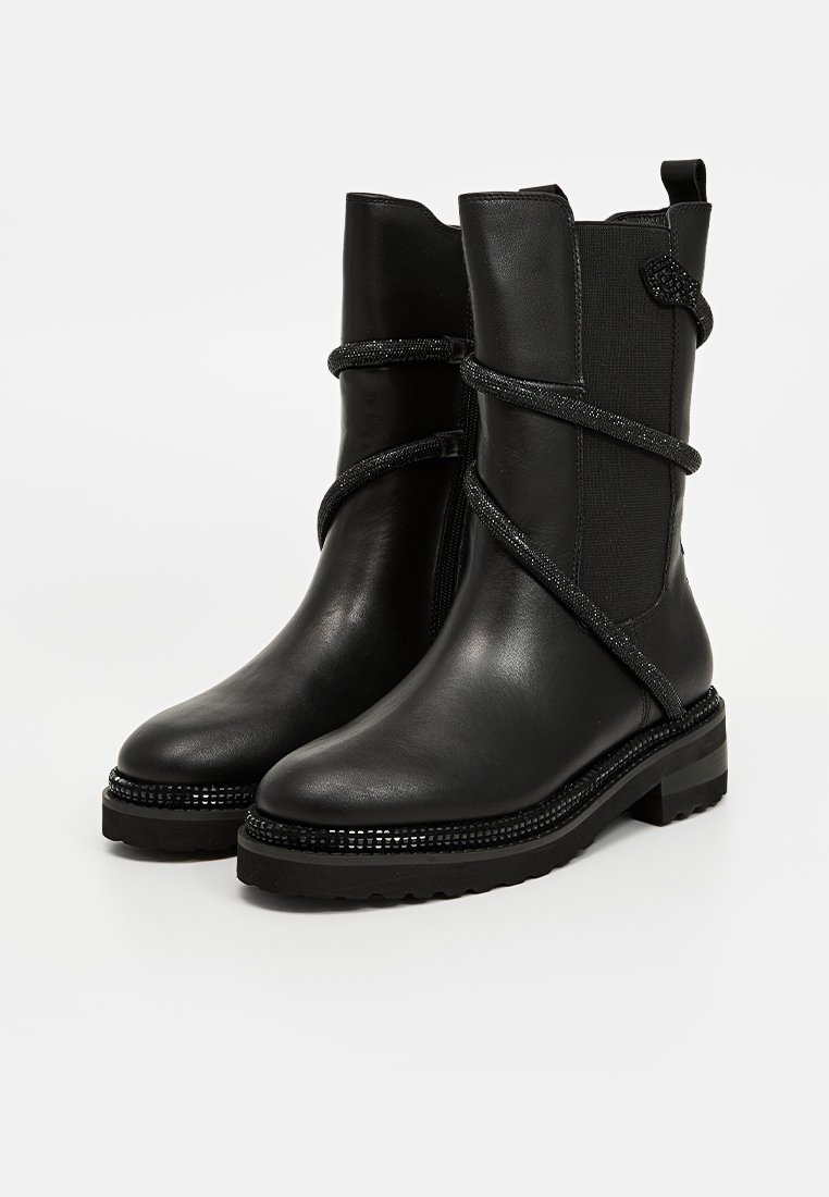 Botas de tobillo de cuero negro con un cuerpo texturizado, que cuentan con una correa decorativa brillante y una suela gruesa y estriada. Diseño de punta redondeada.