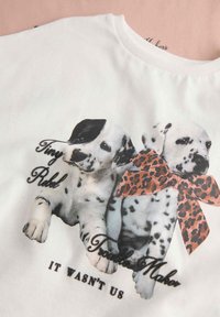 Wit katoenen T-shirt met een afbeelding van twee gevlekte puppy's, waarvan één met een zwarte vlek en een strik met luipaardprint, met tekst eronder.