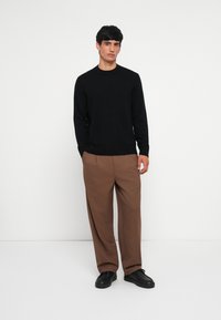 Black long-sleeve sweater, beige trousers, and black shoes. The sweater is fitted with a round neck and the trousers have a loose fit and pleats.