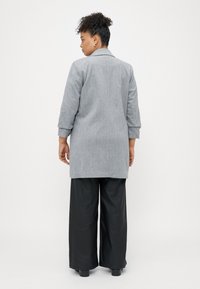Grijs wolmix jas met een op maat gemaakte ontwerp, voorzien van lange mouwen, een notch-kraag en een iets langere achterkant, gecombineerd met zwarte brede broek.