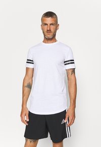 Maglietta bianca a maniche corte con strisce nere sulle maniche, design a girocollo e una texture del tessuto liscia, abbinata a pantaloni corti neri.