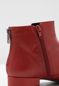 Rote Leder-Ankle-Boots mit strukturierter Oberfläche, seitlichem Reißverschluss mit silbernem Ziehverschluss und flacher schwarzer Sohle.