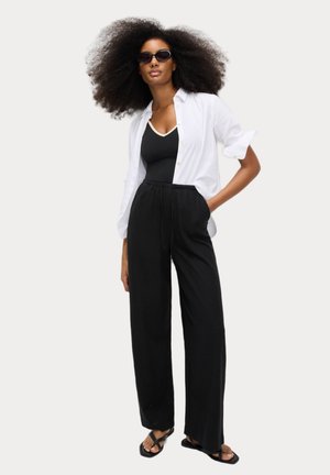 Black wide-leg pants with elastic waistband paired with a white button-up shirt and black tank top. Accessories include black sunglasses.