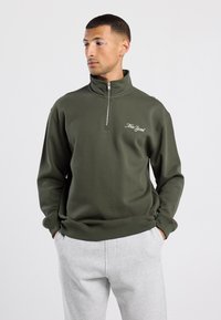 Sudadera de medio cierre en verde oliva con el texto "New York" bordado. Hecha de un tejido suave, cuenta con mangas largas y un corte relajado.