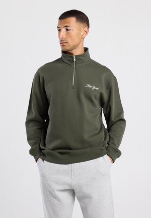 Olive green half-zip pullover with embroidered "New York" text. Made of soft fabric, features long sleeves and a relaxed fit.