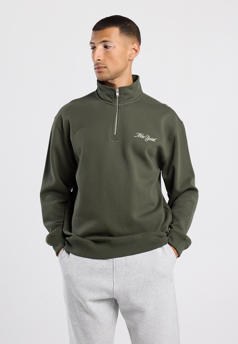 Sudadera de medio cierre en verde oliva con el texto "New York" bordado. Hecha de un tejido suave, cuenta con mangas largas y un corte relajado.