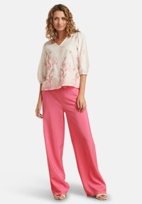 Lichte, beige blouse met roze bloemenborduursels en driekwart pofmouwen, gecombineerd met felroze wijde broek.