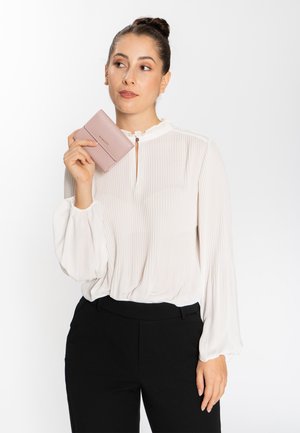Weiße, gefaltete Bluse mit einem Rüschenausschnitt, kombiniert mit schwarzen Hosen. In der Hand wird eine hellrosa Geldbörse gehalten, die aus strukturiertem Material besteht.