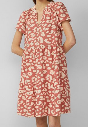 Femme portant une robe ample, à manches courtes, longueur genoux, avec un motif abstrait tacheté rose et crème.