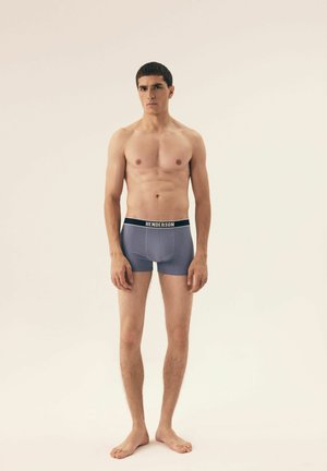Männliche blaue Boxer-Shorts mit einem schwarzen Bund, der weiße Schriftzüge trägt. Glattes Material, enge Passform und Oberschenkellänge.
