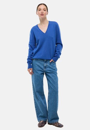 Pull bleu en V en matériau doux, associé à un jean en denim bleu clair taille haute et des chaussures à enfiler texturées.