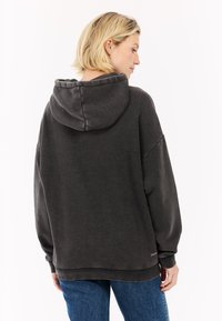 Charcoal grijze oversized hoodie met een gestructureerde afwerking, capuchon en gebreide manchetten, gecombineerd met blauwe jeans. Geen opvallende logo's zichtbaar.